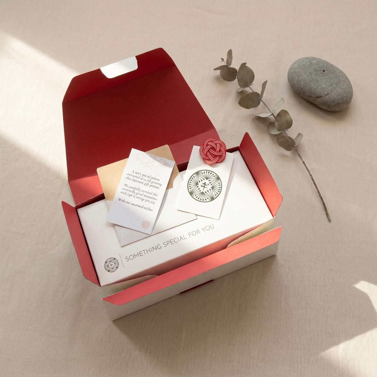 Open red gift box with stationery items on a beige surface